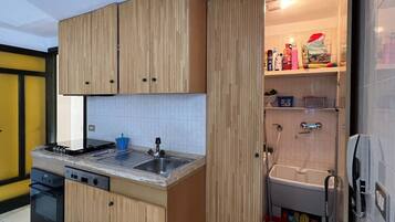 Una cucina compatta con mobili in legno, piano cottura integrato, lavastoviglie e lavello.