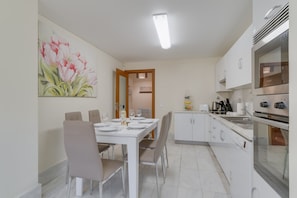 A modern kitchen with white cabinets, a dining table set for four, and a painting of flowers on the wall. - Lido Charm by Atlantic Holiday (Funchal)