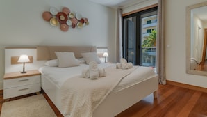 Ein Hotelzimmer mit Bett, Nachttischen, einer Lampe, einer Wanddekoration, einem großen Spiegel und Blick ins Freie.
