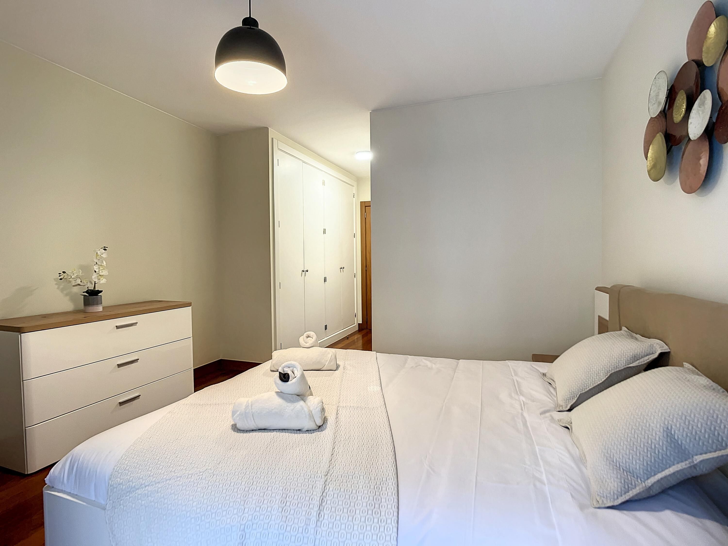 Een keurig opgemaakt slaapkamer met een bed, nachtkastjes, een kledingkast en een hanglamp.