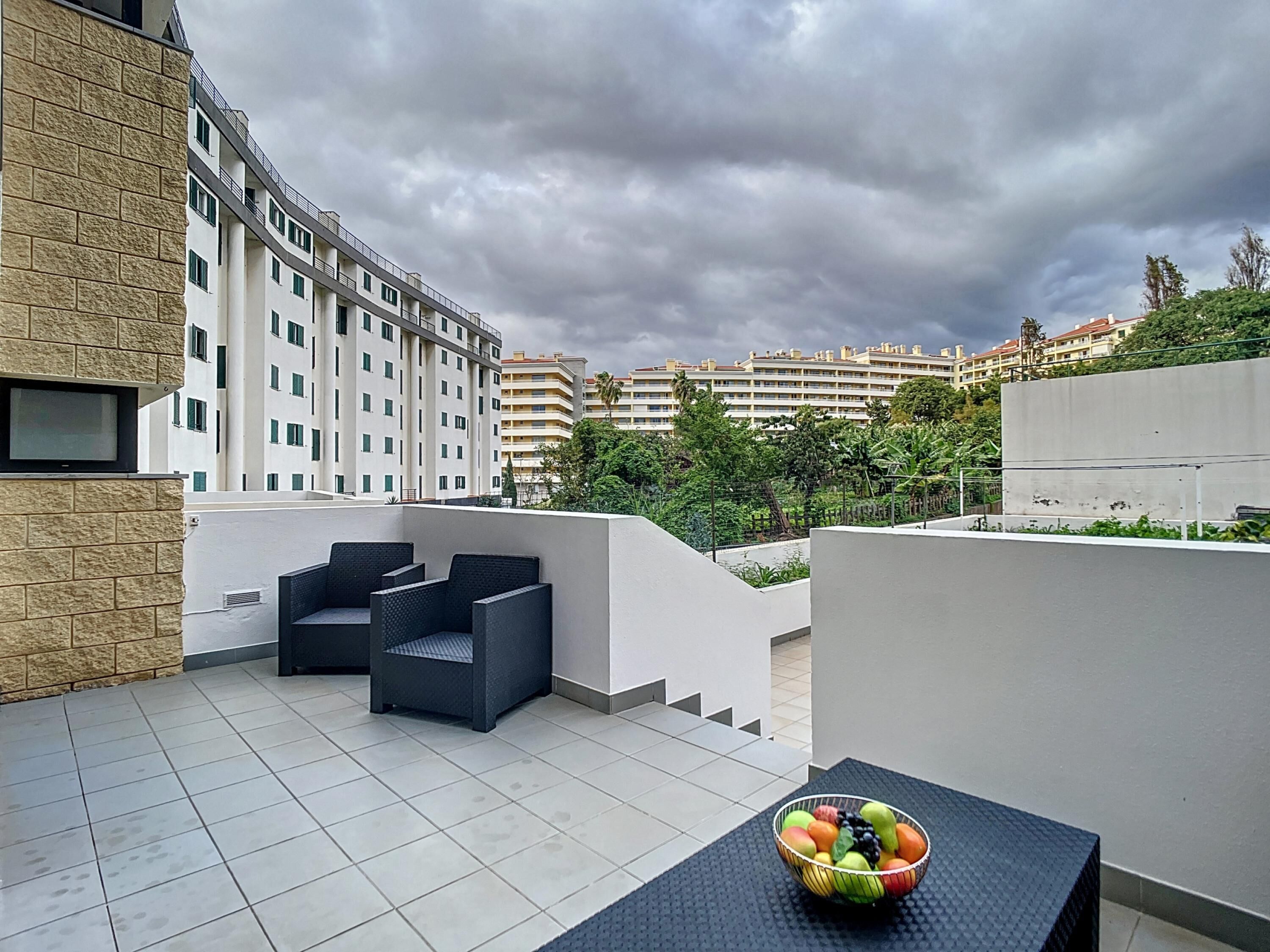 Une terrasse sur le toit, avec une table et des chaises, un saladier rempli de fruits et une vue sur les bâtiments environnants.