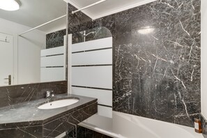 A modern bathroom with a marble sink, a large mirror, and a bathtub.