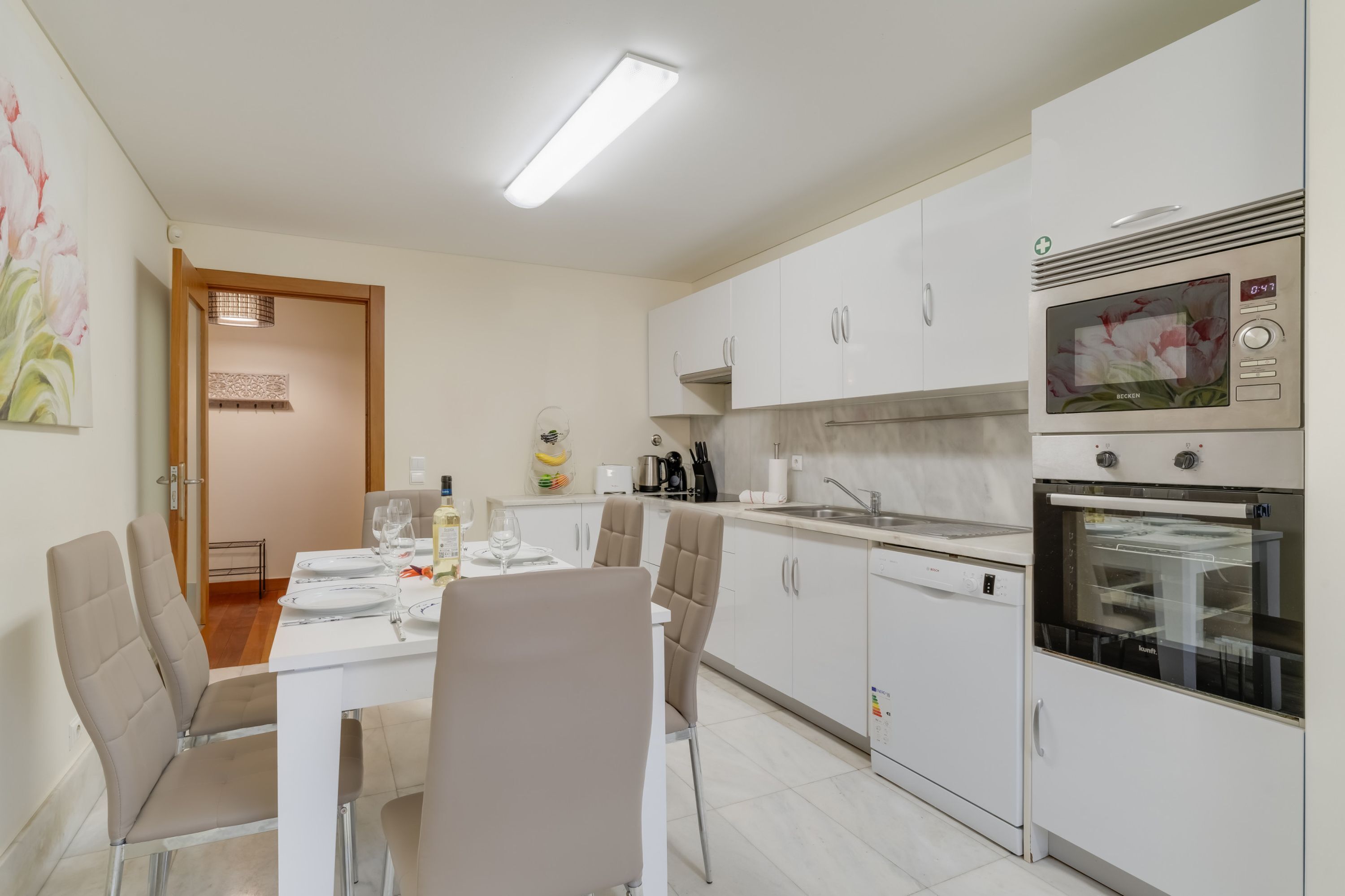 A modern kitchen with white cabinets, a built-in oven, and a dining area with a table set for four.
