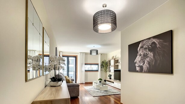 Ein modernes Wohnzimmer mit Holzboden, einem großen Spiegel, einer Topforchidee, einem Sofa, einem Couchtisch und einem Gemälde an der Wand.