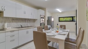 Eine moderne Küche mit weißen Schränken, ein Essbereich mit Tisch für vier Personen und ein Fenster mit Blick auf Grünflächen.