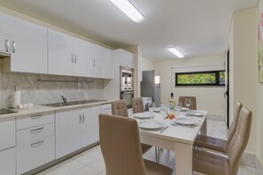 A modern kitchen with white cabinets, a dining area with a table set for four, and a window with a view of greenery. - Lido Charm by Atlantic Holiday (Funchal)