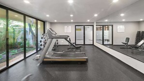 Une salle de sport équipée de tapis de course, d’appareils de musculation et dotée d’une grande fenêtre donnant sur un espace verdoyant.