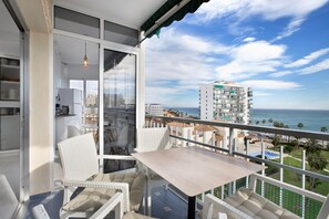 Un balcon avec une table et des chaises, une vue sur l’océan et, au loin, un immeuble de grande hauteur.