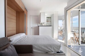 Un dormitorio con cama, sofá, armario de madera, una pequeña kitchenette y un balcón con sillas.