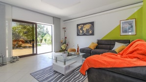 En moderne stue med et glasbord, en grå sofa med orange pude, et verdenskort på væggen og en skydedør af glas, der fører ud til en have.
