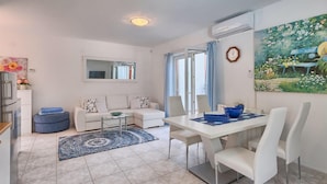 A modern living room with a sofa, a dining table with chairs, a kitchen area with a refrigerator, and a large window with curtains. - Stunning home in Kukci - Nova Vas (Kukci - Nova Vas)