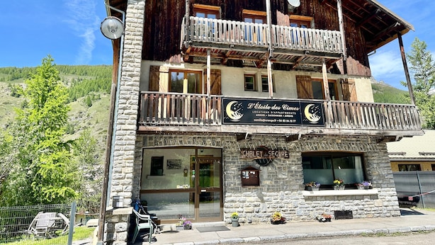 Un bâtiment à deux étages doté d’un balcon en bois, d’une enseigne indiquant qu’il s’agit d’un établissement d’hébergement, et offrant une vue sur le paysage environnant.