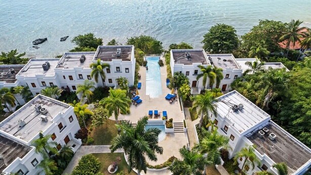 Un resort con varias edificaciones blancas, una piscina central y palmeras.