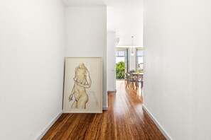 Un pasillo con una obra de arte enmarcada, suelo de madera y una zona de comedor al fondo.