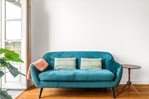 Un canapé en velours turquoise agrémenté de coussins à rayures, une petite table ronde en bois et une grande plante verte.