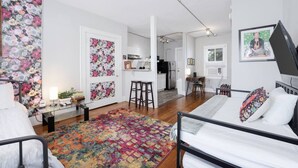 A modern, well-lit room with a bed, a desk, and a chair. There is a kitchen area in the background with a refrigerator and a stove. - ArtMusicEntertainment+Downtown+PetsOK+Walk2Shore (Corpus Christi)