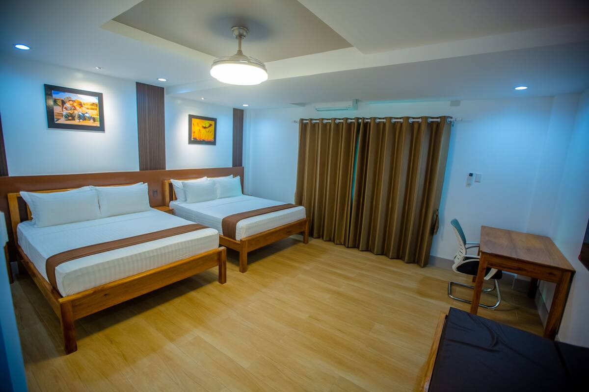 A hotel room with two wooden beds, a desk, and a chair.