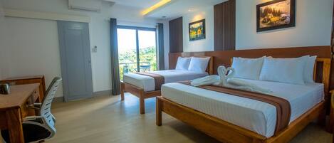 A hotel room with a large bed, a desk, and a chair. There is a balcony with a view of the outdoors.