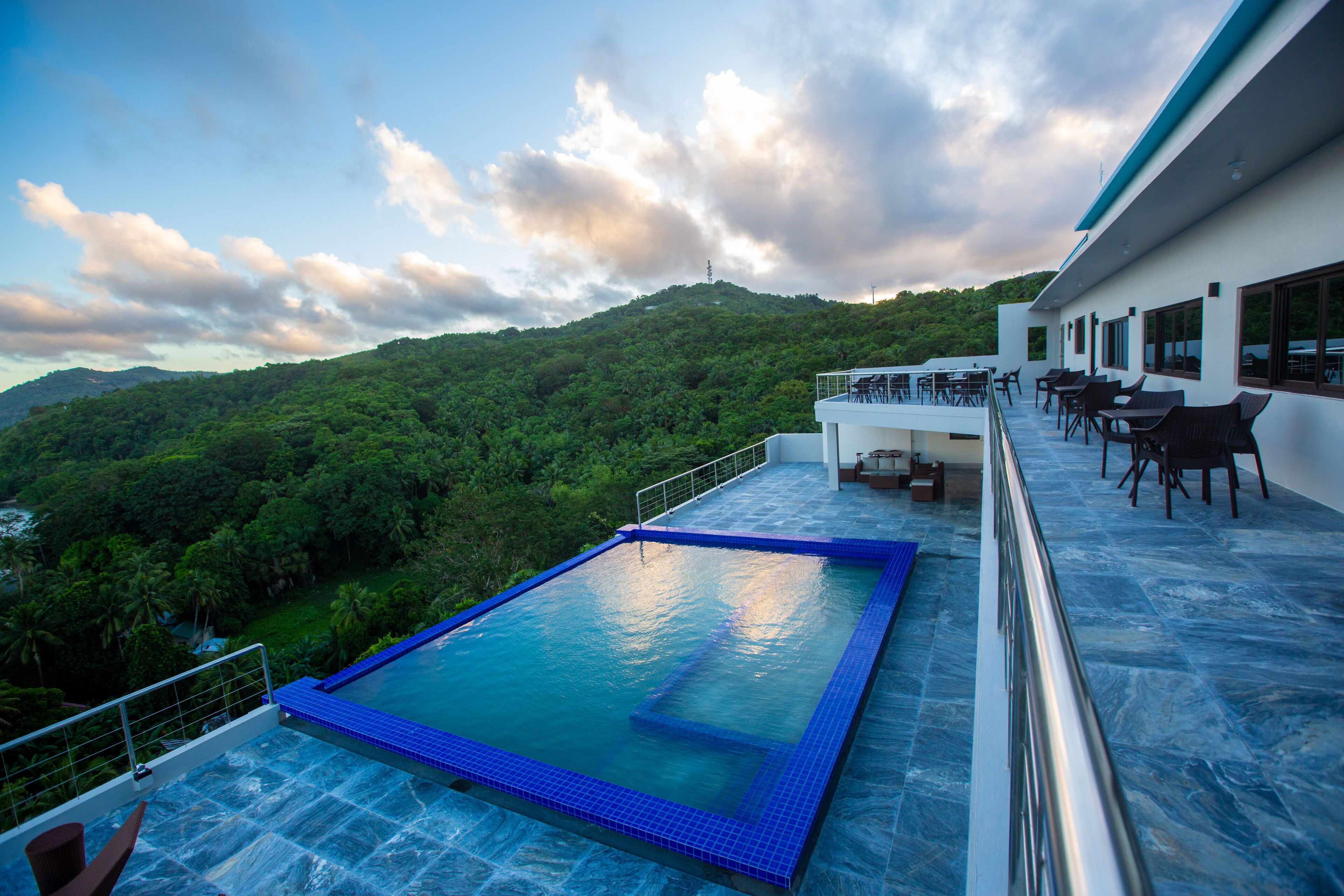Une piscine à débordement située sur le toit, offrant une vue sur une végétation luxuriante et une colline.