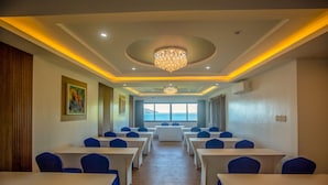 Un salón de conferencias con mesas y sillas, una araña y vistas al mar.