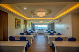 Un salón de conferencias con mesas y sillas, una araña y vistas al mar.