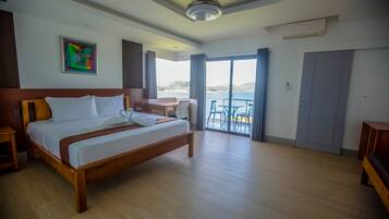 Une chambre d’hôtel avec un lit en bois, une petite table, une chaise et une vue sur la mer grâce à de grandes fenêtres.