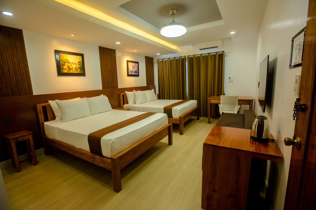 A hotel room with two wooden beds, a small table, a TV, and a ceiling light.