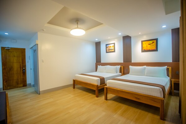 A hotel room with two wooden beds, a ceiling fan, recessed lighting, and a wooden door.