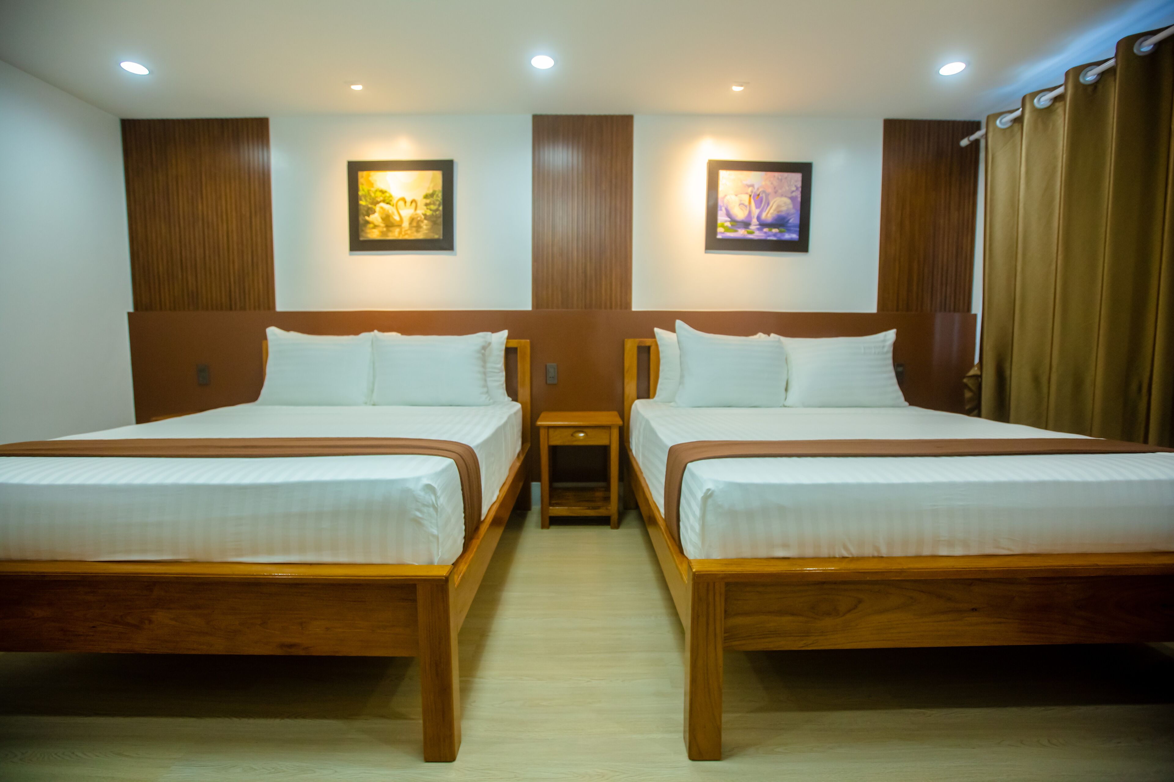 Habitación de hotel con dos camas individuales, cabeceros de madera, ropa de cama blanca, mesitas de noche pequeñas y dos cuadros colgados en la pared.