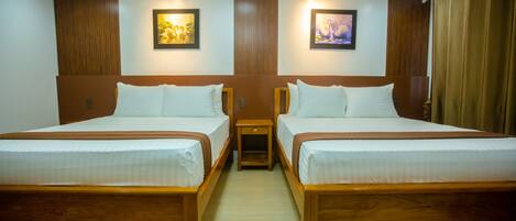 Habitación de hotel con dos camas individuales, cabeceros de madera, ropa de cama blanca, mesitas de noche pequeñas y dos cuadros colgados en la pared.