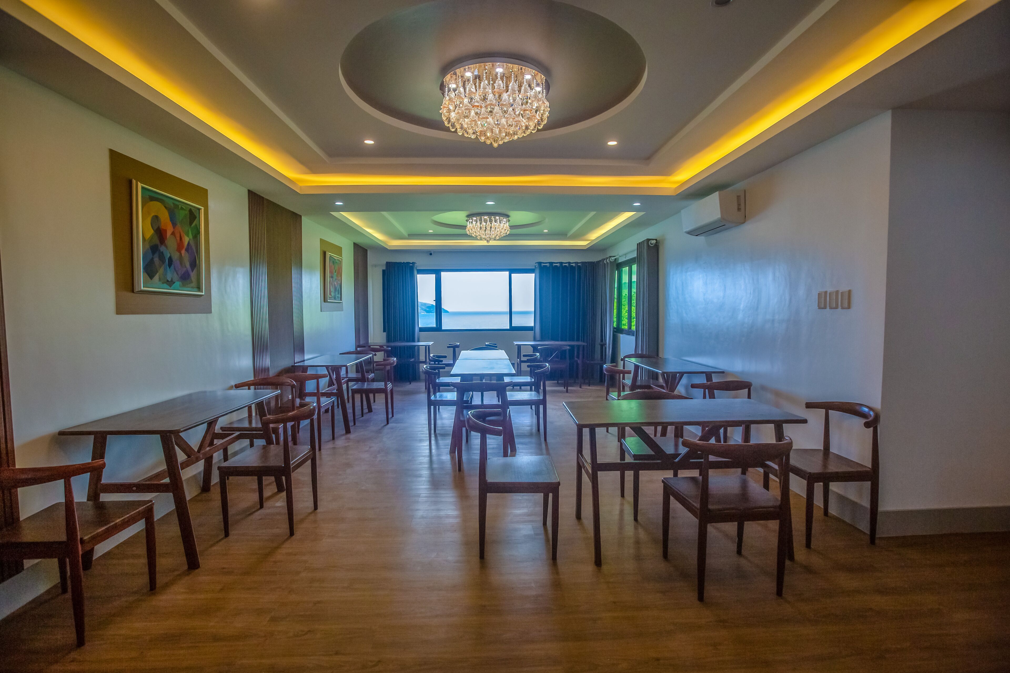 A spacious dining area with wooden tables and chairs, a chandelier, and artwork on the walls.