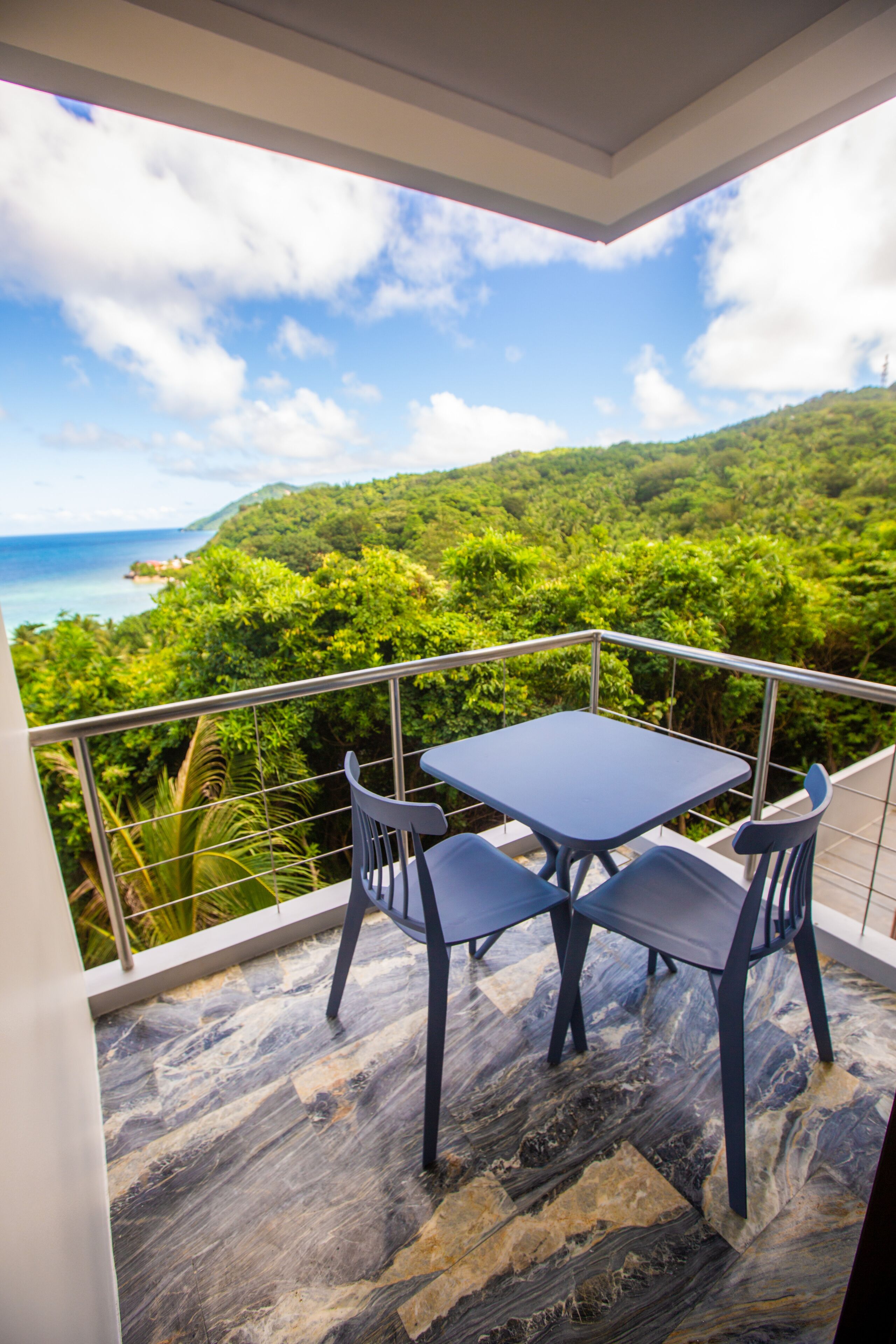 A balcony with a table and chairs, overlooking a lush green landscape and the sea.
