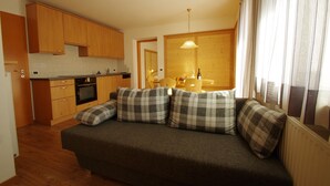 A compact living space with a kitchenette, a sofa with plaid cushions, and a dining area with a table and chairs. - Apartment 'Villa Hubertus Valtoi' with Mountain View, Balcony and Wi-Fi (Ortisei (BZ))