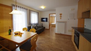 A modern kitchen with wooden cabinets, a dining area with a table and chairs, a sofa, and a television mounted on the wall. - Apartment 'Villa Hubertus Valtoi' with Mountain View, Balcony and Wi-Fi (Ortisei (BZ))