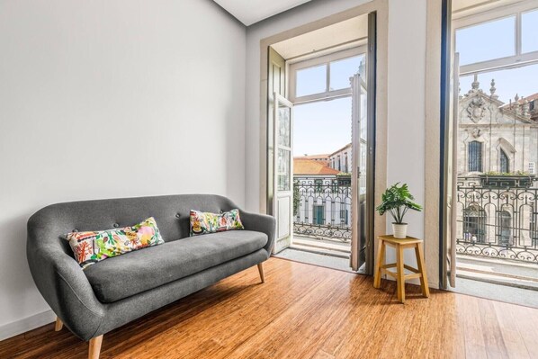 A modern living room with a grey sofa, colorful cushions, a wooden stool, and a potted plant.