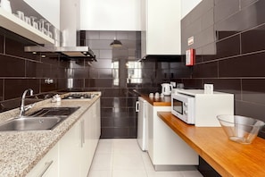 A modern kitchen with a granite countertop, stainless steel appliances, and black tiled walls.