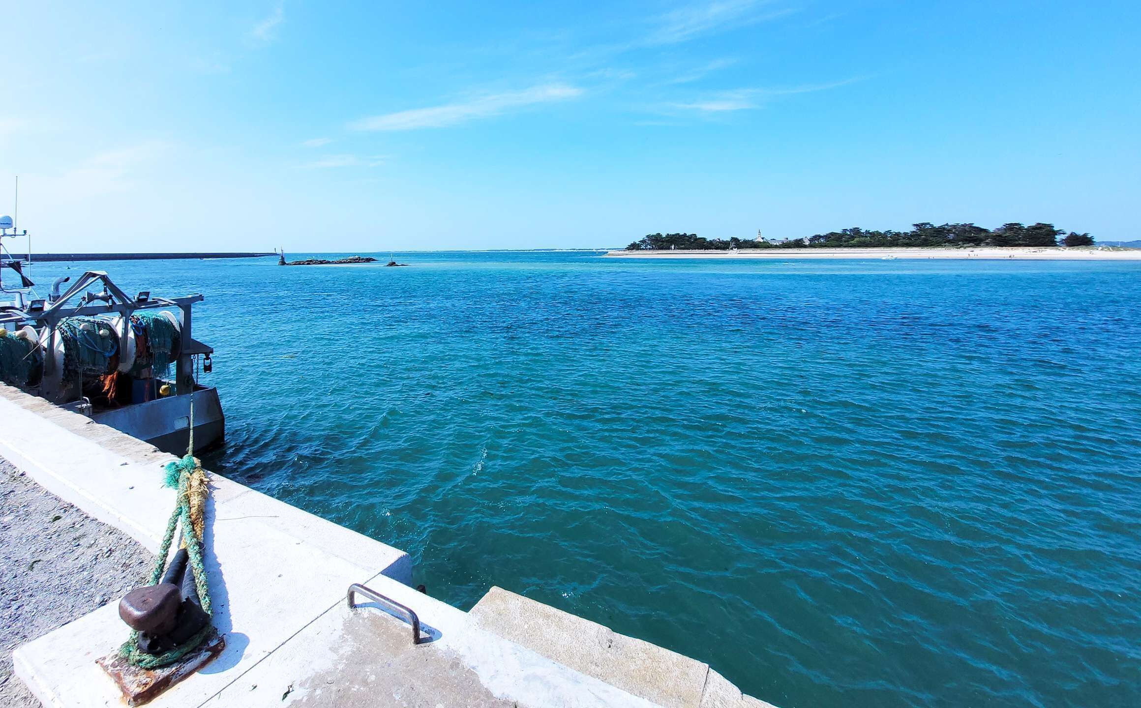 A boat docked at a pier with clear blue water and a distant island.