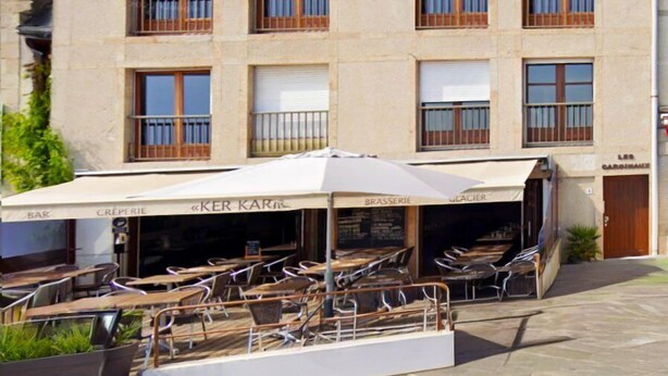 Un immeuble doté de nombreux balcons, un café avec une terrasse, et une devanture de magasin avec une enseigne.