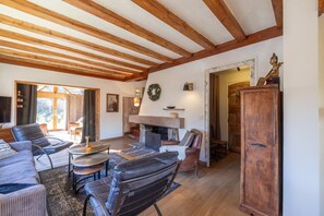 Un salon spacieux doté d’une cheminée, de poutres apparentes au plafond et d’une grande armoire en bois.