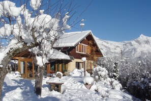 A wooden chalet with a sloped roof, surrounded by snow-covered trees and mountains in the background. - Chalet Le Solli – Panoramic View of the Mont-Blanc Range (Saint gervais les bains)