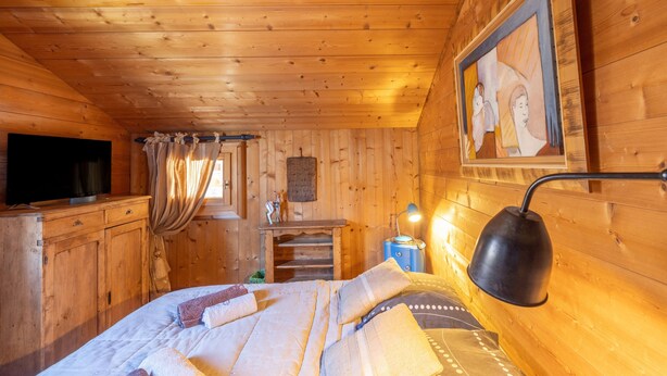 Une chambre dans une cabane en bois, avec un lit, un bureau, une télévision et un tableau accroché au mur.