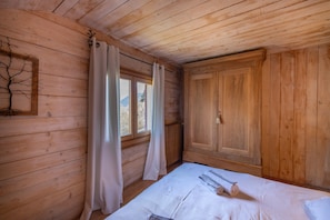 A wooden room with a bed, a radiator, and a window with curtains.