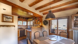 Une cuisine rustique avec des poutres en bois, une table à manger avec des chaises et une vue par la fenêtre.