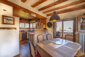 A rustic kitchen with wooden beams, a dining table with chairs, and a view through the window. - Chalet Le Solli – Panoramic View of the Mont-Blanc Range (Saint gervais les bains)