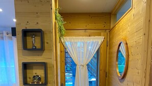 Un intérieur en bois avec une porte donnant sur l’extérieur, une petite étagère avec un livre et un miroir accroché au mur.
