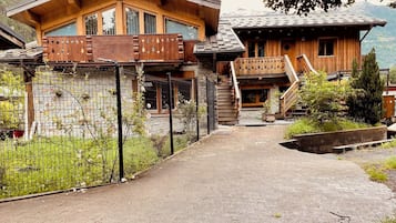 A wooden chalet with a stone facade, a wooden balcony, and a staircase leading to a second level.