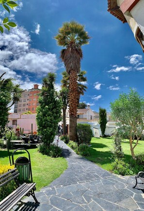 Stroll through the tranquil courtyard, surrounded by lush greenery and a traditional building with a pitched roof.