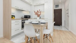Une cuisine moderne avec des meubles blancs, une table à manger dressée pour quatre personnes et un vase rempli de fleurs.