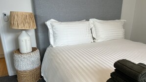Un lit bien fait, avec une literie blanche, une lampe et un panier en osier posé sur un tapis.