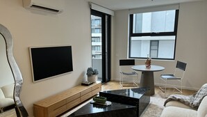 Un salon moderne doté d’un téléviseur à écran plat, d’une table basse en marbre, d’un canapé, d’un banc et d’un coin repas comprenant deux chaises et une petite table.